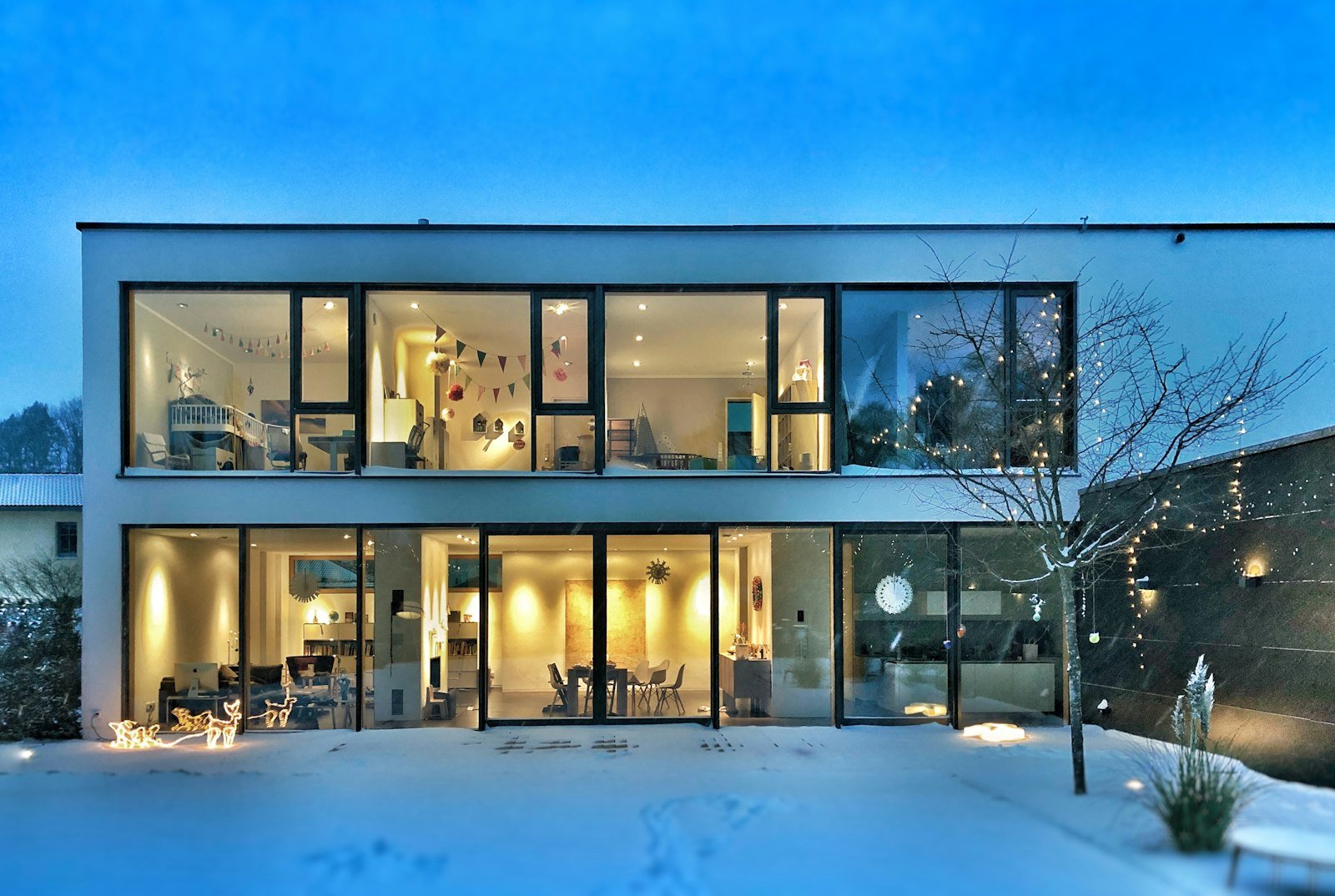Modernes zweigeschossiges Wohnhaus mit Flachdach und großen Glasfronten im Winter, Räume von innen beleuchtet